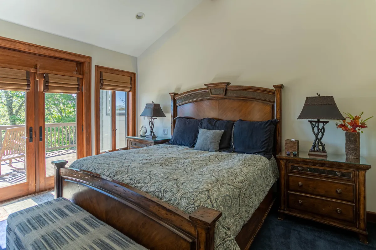 A spacious bedroom featuring a luxurious king-sized bed adorned with high-end linens, complemented by warm wooden furniture and softly glowing lamps. Doors reveal a scenic view of the outdoors, filling the room with natural light and offering a tranquil setting for relaxation.