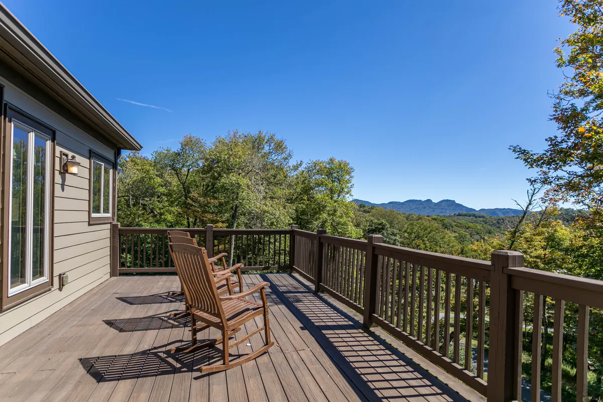 This image features a pair of wooden rocking chairs on a spacious deck, overlooking a sweeping mountain view beyond the deck railing. The scene is tranquil, with soft natural light and the suggestion of enjoying the outdoors, whether sipping morning coffee or relaxing after a day on the slopes.
