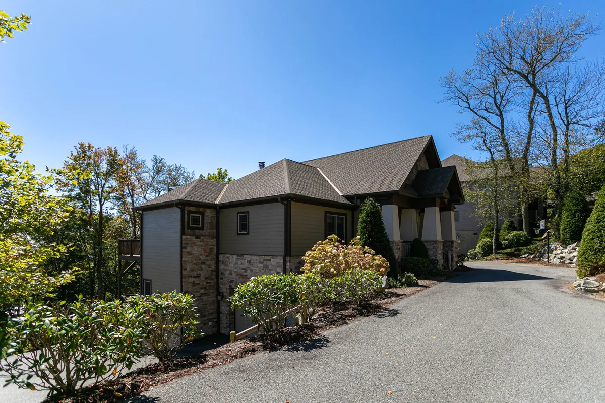 An exterior view of the property’s stone facade and landscaped bushes, with a welcoming driveway leading up to the home and a glimpse of the scenic porch area. The setting is tranquil and hints at the mountain retreat experience, making it easy to imagine arriving after a day of adventure.