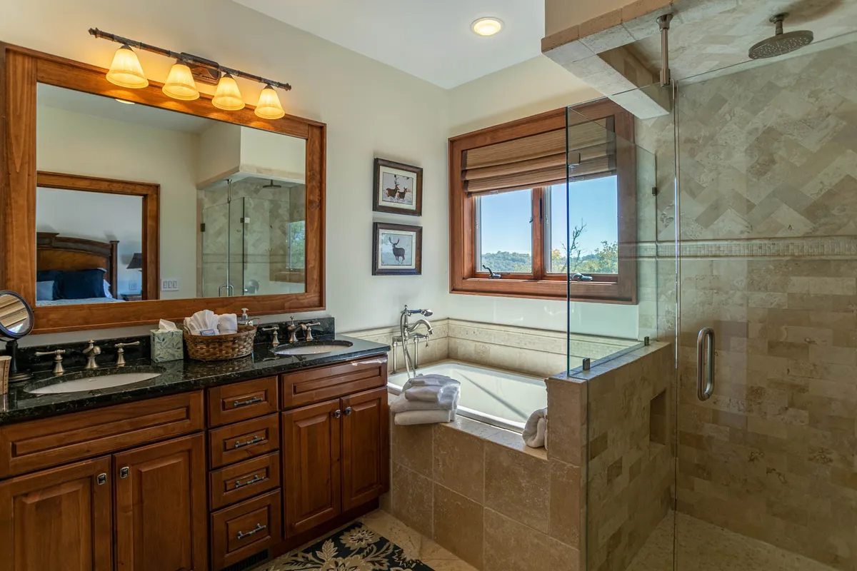 A spa-inspired bathroom with a sleek double sink vanity, a spacious walk-in shower, and a standalone soaking bathtub. Abundant natural light pours in through the window, underscoring the room's serene and opulent character.