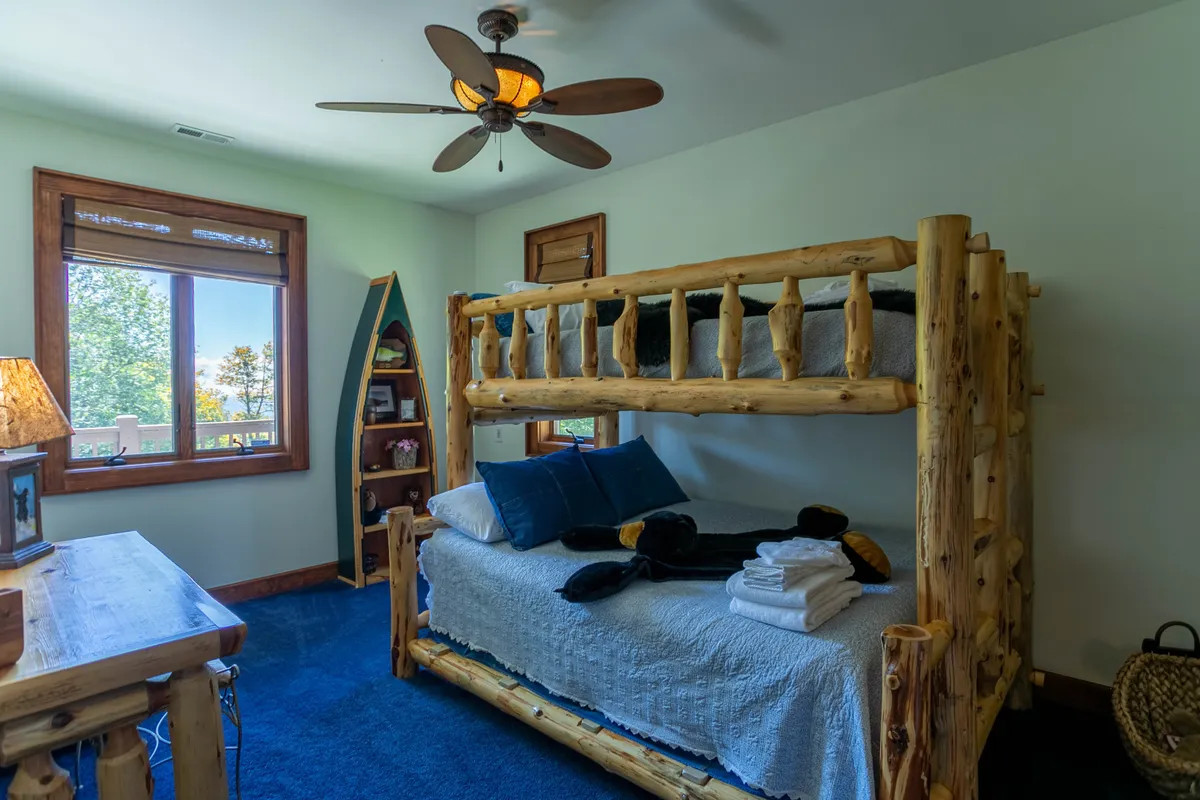 A playful bunk room designed for younger guests, featuring a sturdy bunk bed, desk space for activities or studying, and a window letting in natural light. Decorative shelving adds a whimsical touch, making the space welcoming and fun.