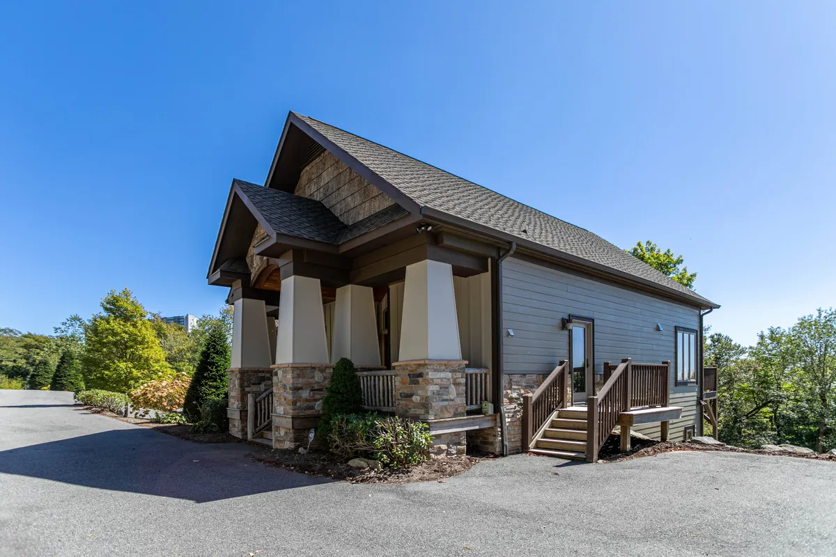 The front exterior of Heart Rock Lodge is showcased here, with a striking stone facade, a welcoming gabled roof, wooden steps, and manicured landscaping. The space suggests gatherings on the porch and relaxing moments outdoors.